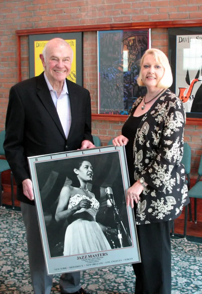 Pictured: Stan Levenson (left) holding a framed jazz poster with Joanna St. Angelo (right)